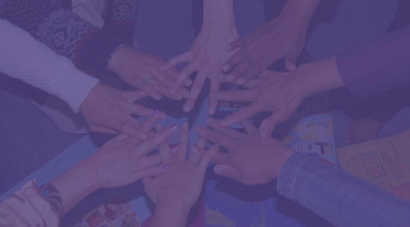 Image has a purple filter over it, but shows a group of hands in a circle,