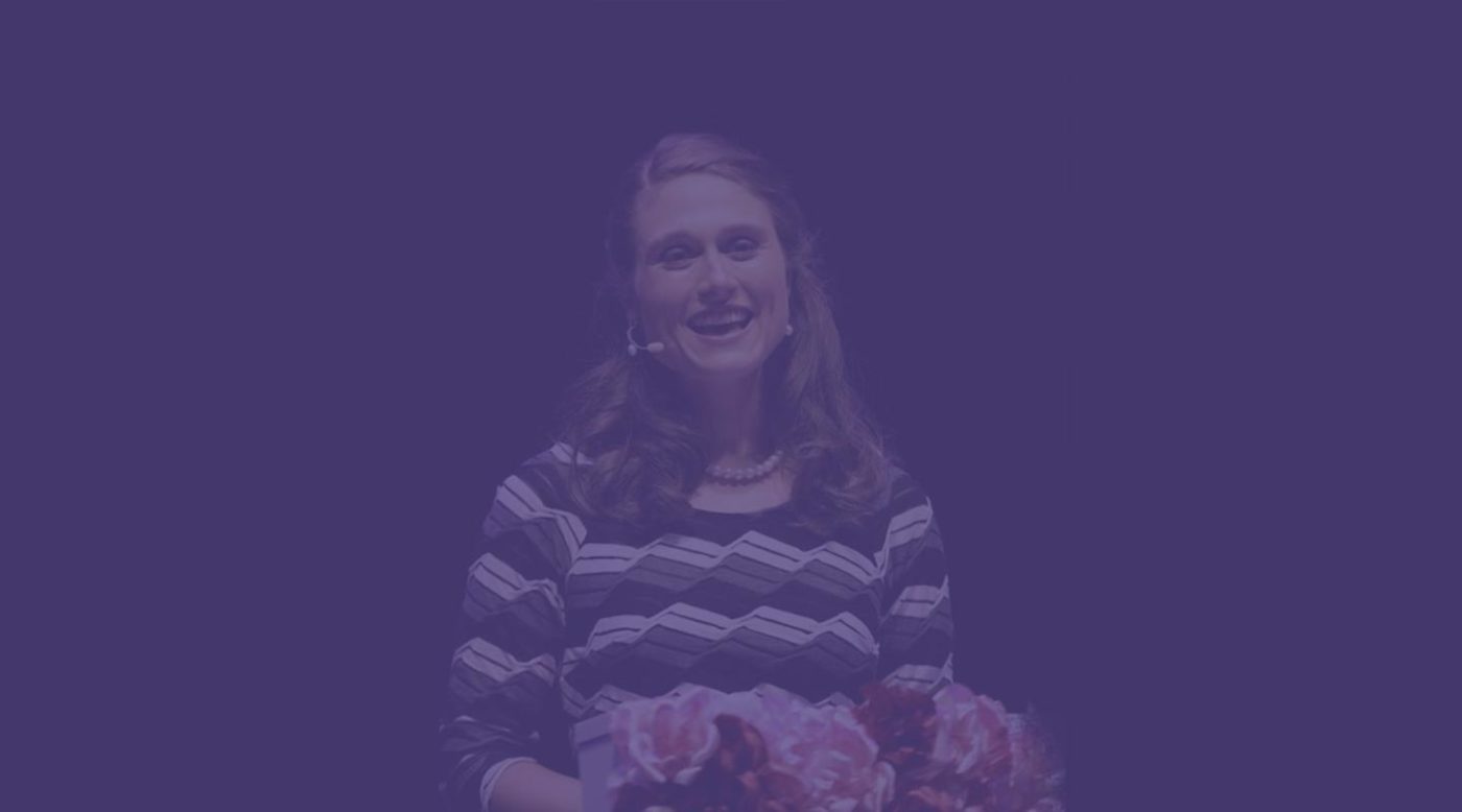 Image has a purple filter over it, but shows a person speaking.